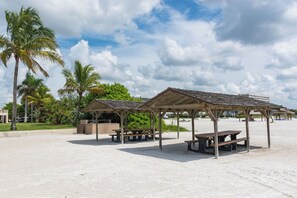 A beach with two wooden gazebos, picnic tables, and palm trees.