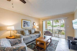 A living room with a sofa, armchair, coffee table, and a TV. There is a window with a view of greenery outside. - Comfortable one bedroom 1.5 bathroom condominium (Sarasota)