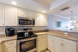 A modern kitchen with stainless steel appliances, white cabinetry, granite countertops, and pendant lighting.