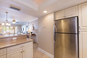 A kitchen with a stainless steel refrigerator, granite countertops, and white cabinetry. - Comfortable one bedroom 1.5 bathroom condominium (Sarasota)