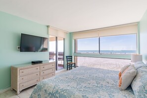 A bedroom with a bed, dresser, TV, and a view of the beach.