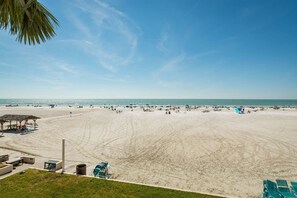 A beach with a gazebo, lounge chairs, and a clear sky.