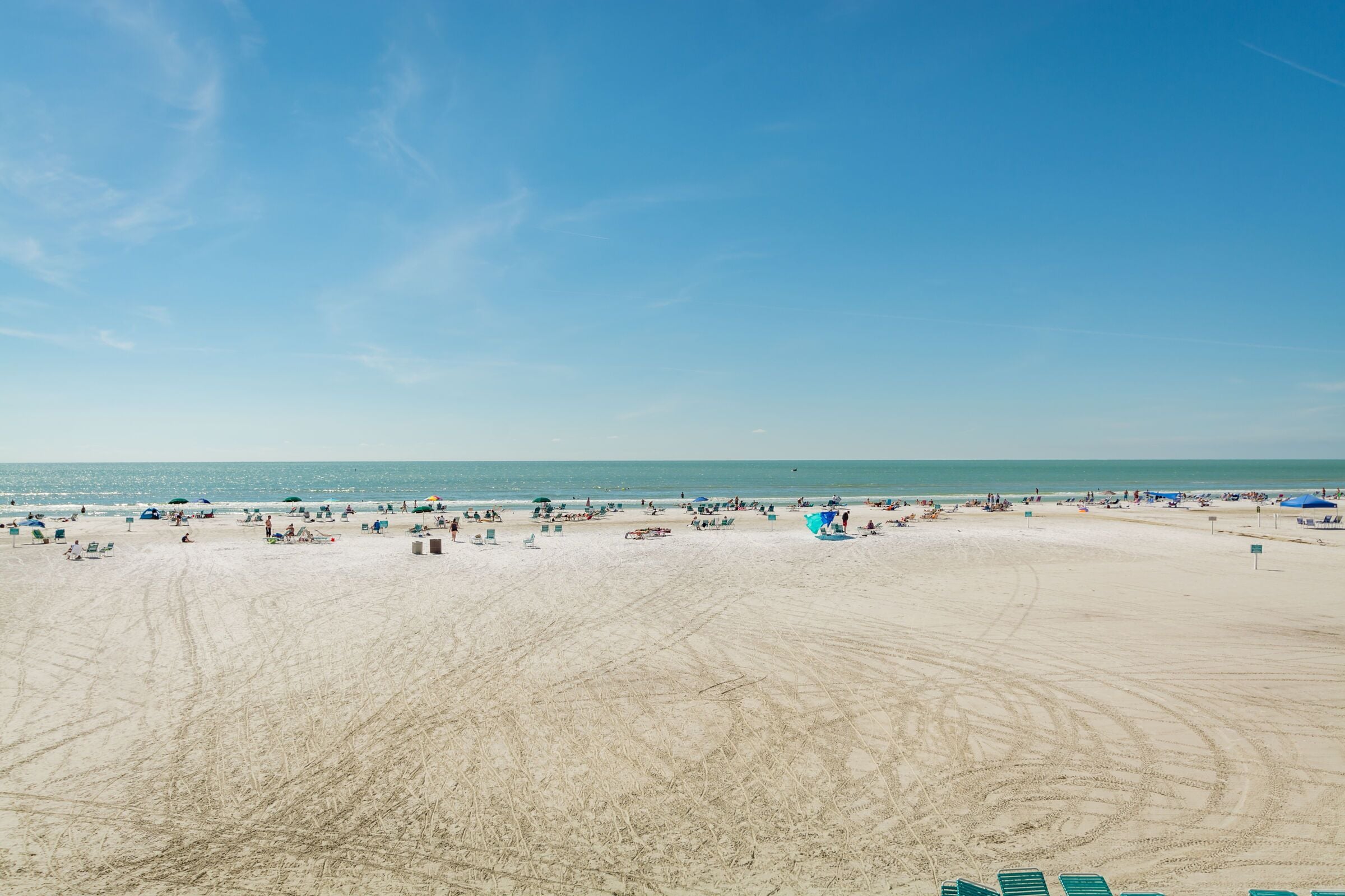 Une vaste plage de sable où l’on voit des gens et des parasols, un ciel dégagé et l’océan en arrière-plan.