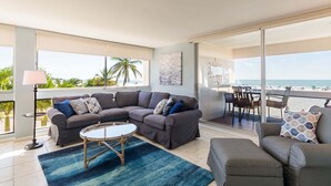 Una sala moderna con un sofá grande, una mesa de centro y vistas a la playa.