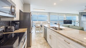 Une cuisine moderne dotée d’un grand îlot central, d’appareils électroménagers en acier inoxydable et offrant une vue sur l’océan.