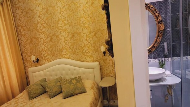 A bedroom with a patterned wallpaper, a white headboard, and a bed with green pillows. - Economic Double rooom (Roma)