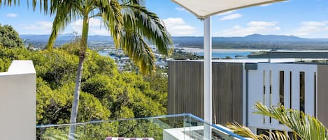 A balcony with a view of a coastal landscape, including a body of water and distant mountains.