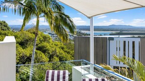 Un balcon offrant une vue sur un paysage côtier, comprenant une étendue d’eau et des montagnes lointaines.