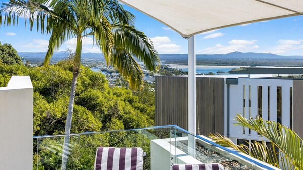 A balcony with a view of a coastal landscape, including a body of water and distant mountains.