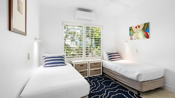 A bedroom with two single beds, a window with blinds, a ceiling fan, and a wall-mounted air conditioner. - Upper Hastings Penthouse 5 Noosa Heads (Noosa Heads)