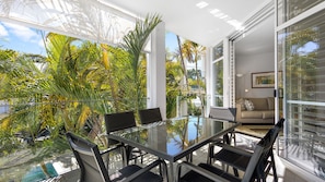 A modern indoor space with a glass table and chairs, surrounded by tropical plants and large windows. - Upper Hastings Penthouse 5 Noosa Heads (Noosa Heads)