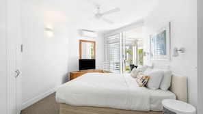 A modern bedroom with a bed, a television, and a window with blinds.