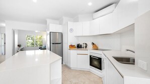 A modern kitchen with white cabinetry, a stainless steel refrigerator, a built-in oven, and a large island. - Upper Hastings Penthouse 5 Noosa Heads (Noosa Heads)