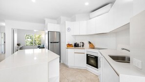 A modern kitchen with white cabinetry, a stainless steel refrigerator, a built-in oven, and a large island. - Upper Hastings Penthouse 5 Noosa Heads (Noosa Heads)