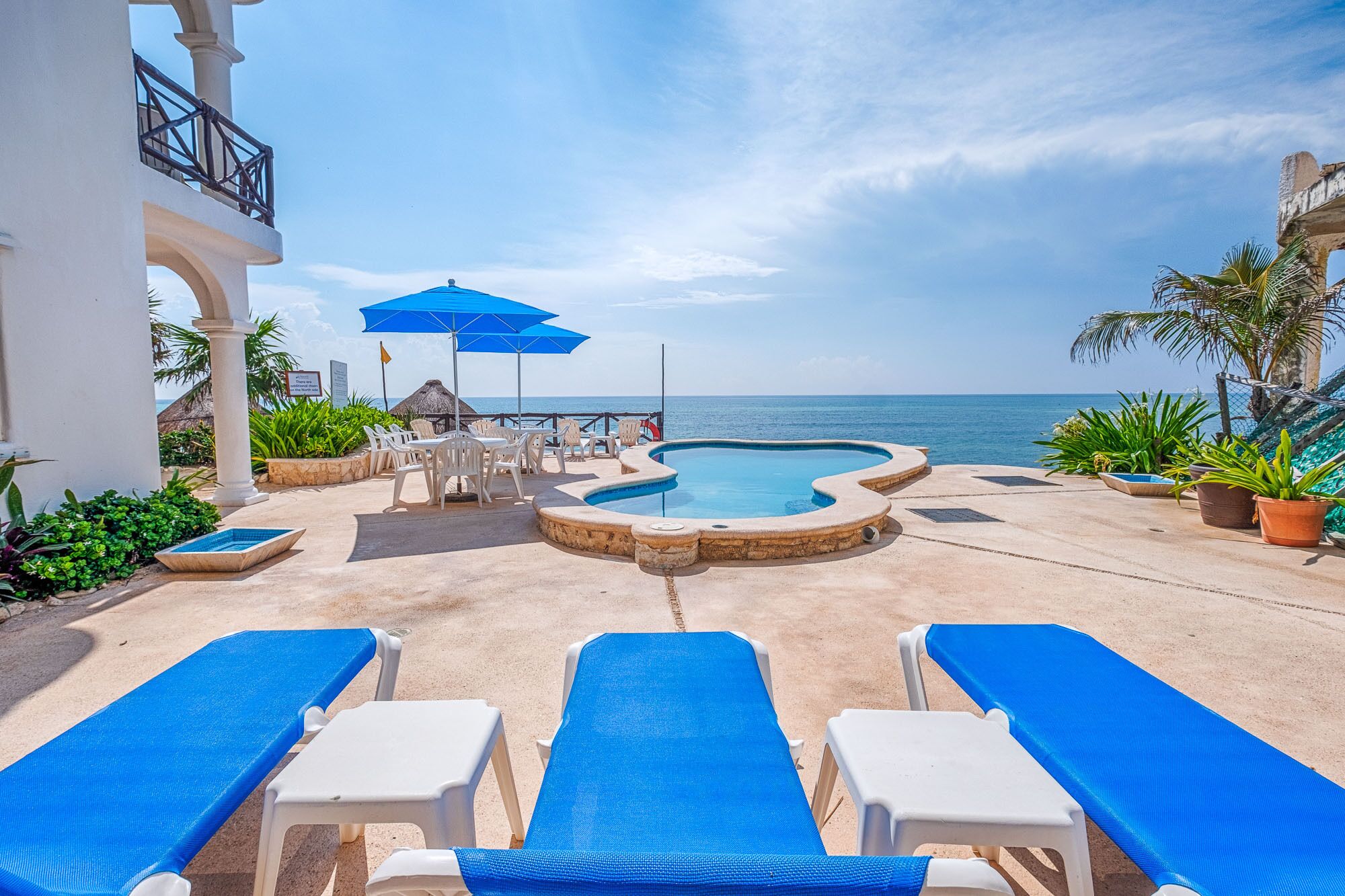 Un área junto a la piscina con sillones, piscina y vista al océano.