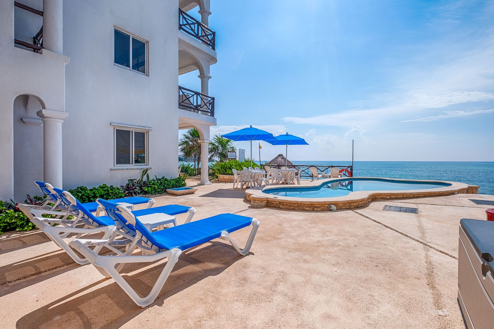 A pool area with lounge chairs and umbrellas, a small pool, and a view of the sea.