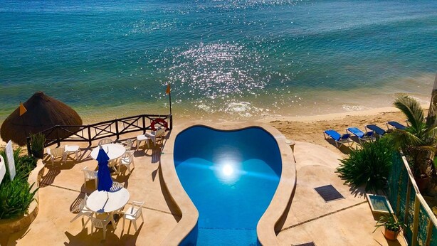 Une vue sur la piscine, avec une vue dégagée sur l’océan, des chaises longues et un parasol en feuilles de palmier.