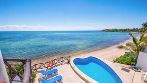 A beachside pool area with clear blue water, a sandy beach, and a view of the ocean. - Newly Updated Beachfront Condo with Terrace, Pool & Daily Service (Akumal)