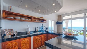 A kitchen with a large island, wooden cabinets, and a view of the ocean. - Newly Updated Beachfront Condo with Terrace, Pool & Daily Service (Akumal)