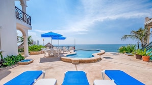 A poolside area with lounge chairs, a pool, and a view of the ocean. - Oceanview Condo with Balconies, Pool & Daily Service (Akumal)