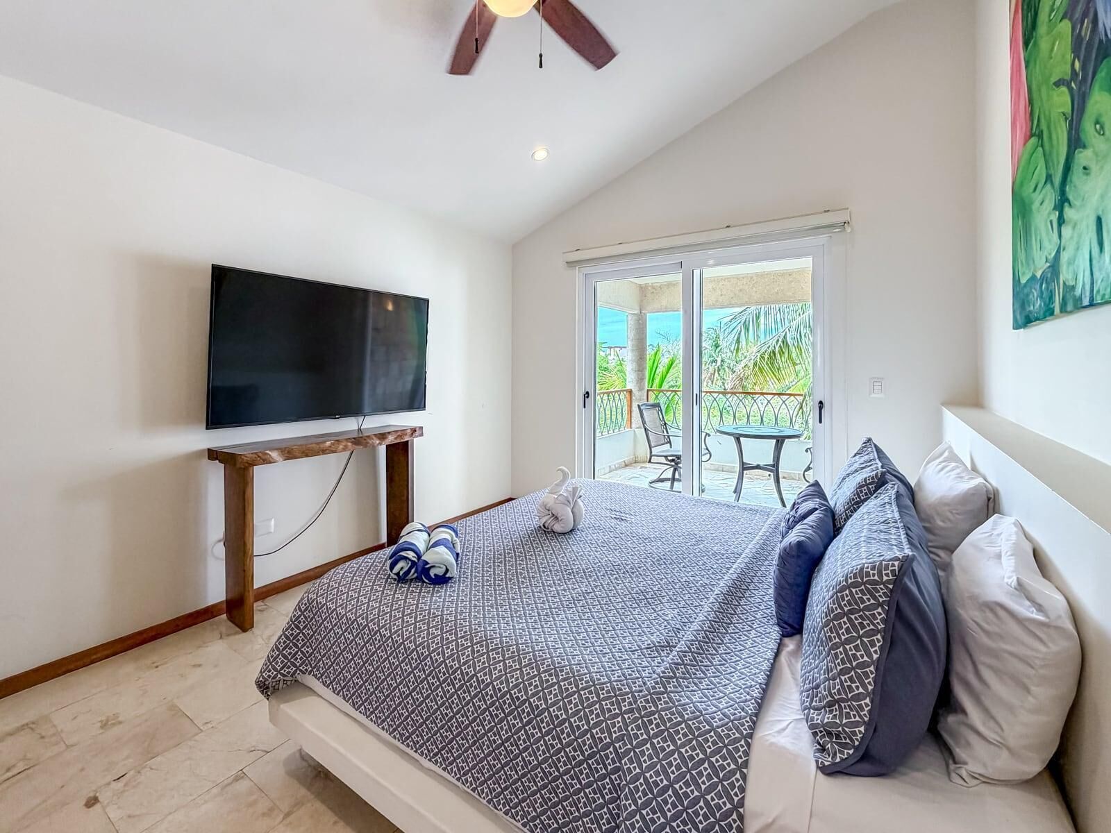 Une chambre à coucher avec un lit, un téléviseur fixé au mur et un balcon équipé d’une table et de chaises.