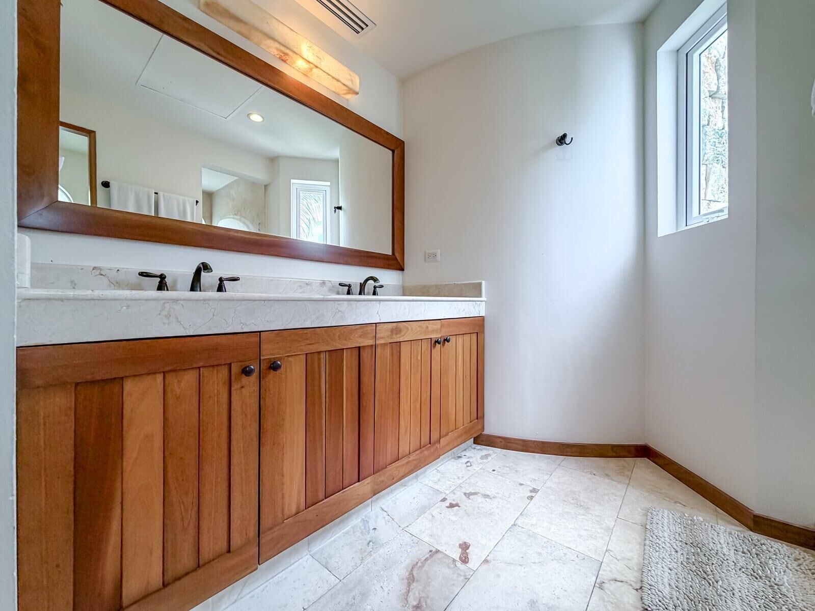 Une salle de bain avec un meuble-lavabo en bois, un grand miroir et une fenêtre.