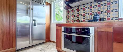 A kitchen with a stainless steel refrigerator, a built-in oven, wooden cabinets, and a patterned backsplash.