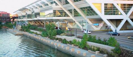 A modern building with a unique angular design, located beside a river with a pedestrian walkway and greenery.