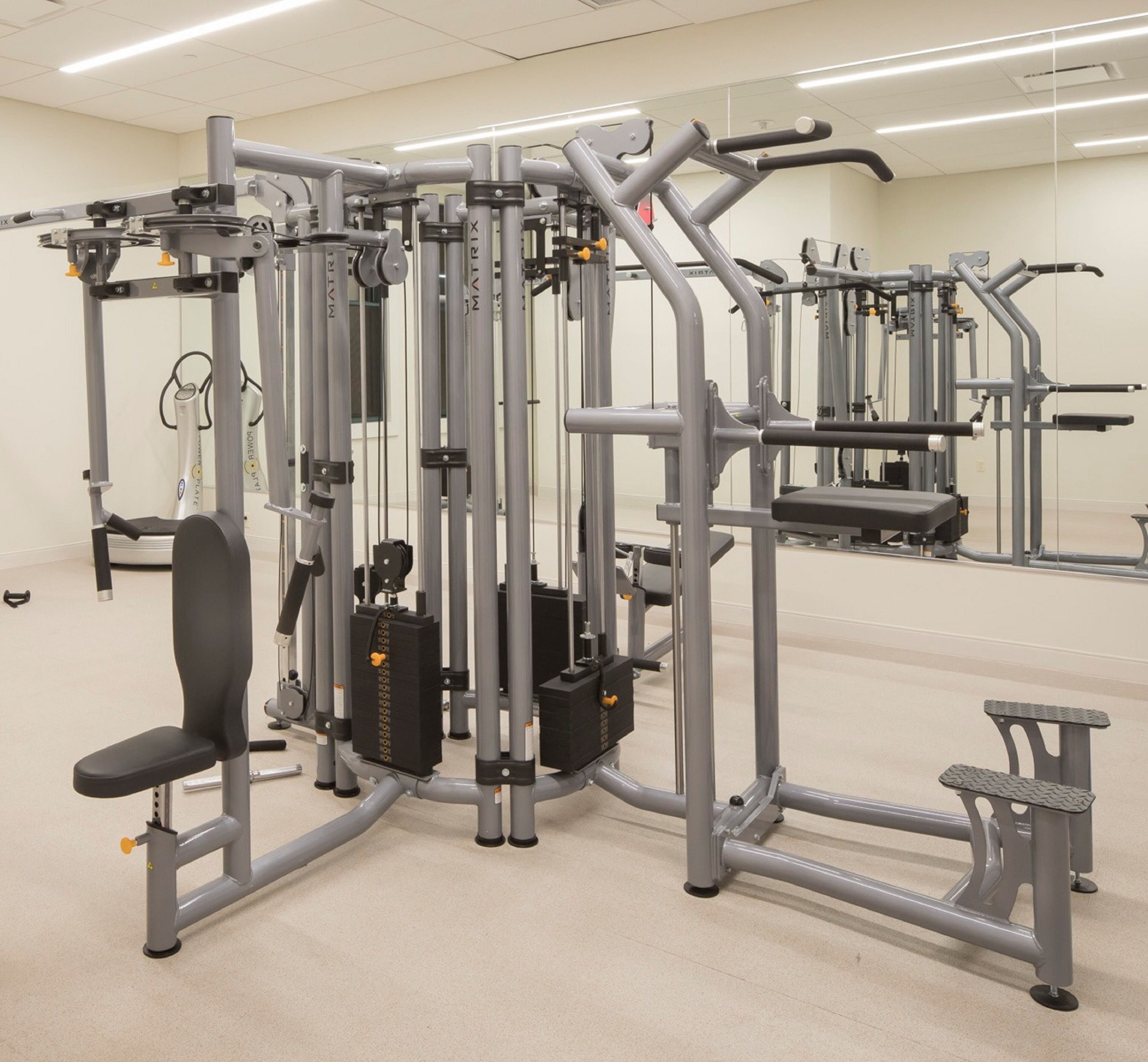 A gym with various exercise machines, including a bench press, a cable machine, and a leg press.