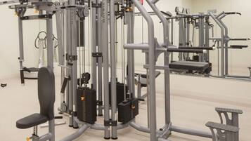 A gym with various exercise machines, including a bench press, a cable machine, and a leg press.