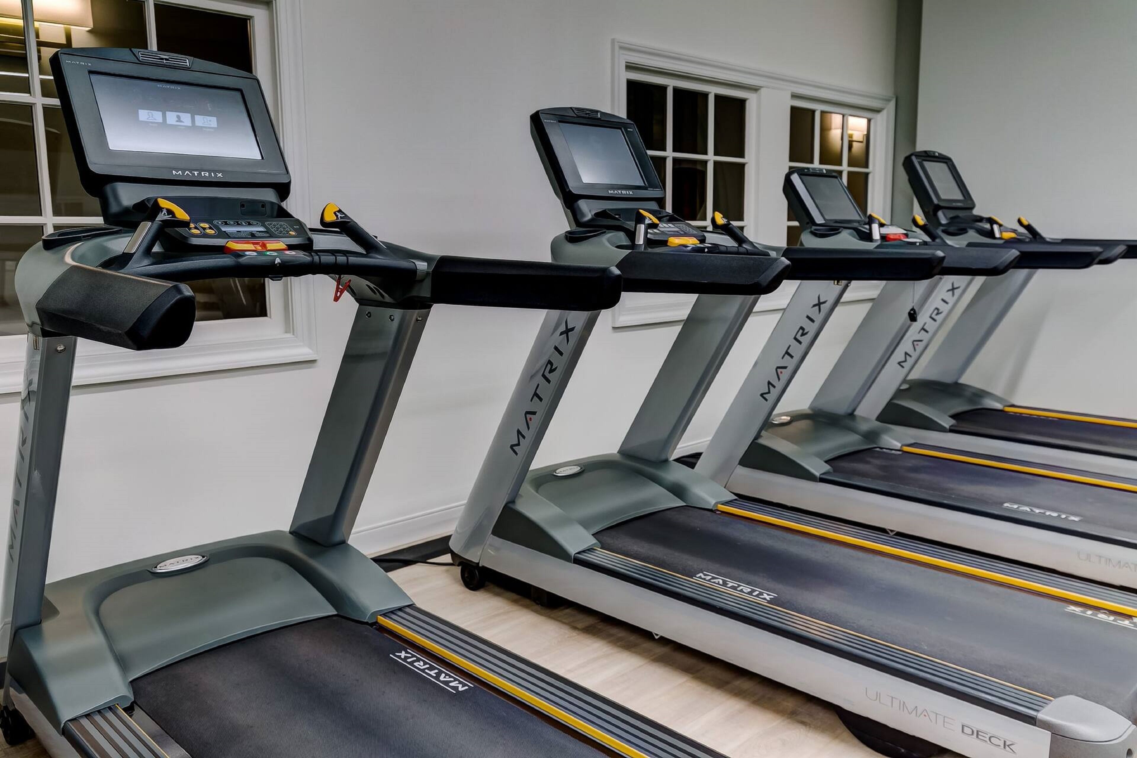 Four treadmill machines with digital displays, labeled MATRIX, in a room with white walls and a window.