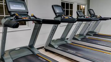 Four treadmill machines with digital displays, labeled MATRIX, in a room with white walls and a window.