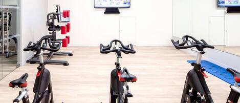 A gym with stationary bikes, a weight machine, and a wall-mounted TV.