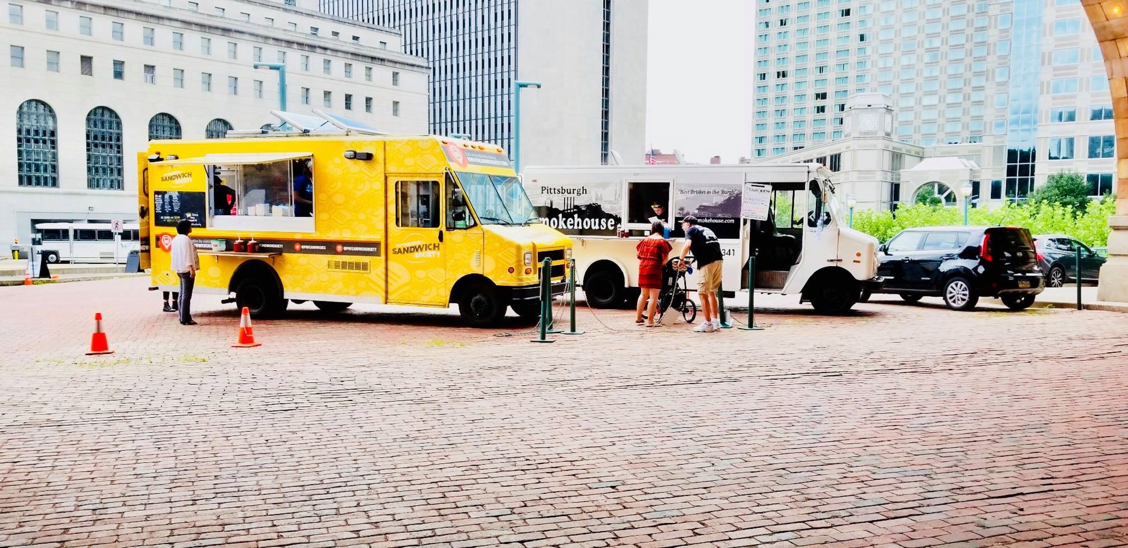 A yellow food truck parked on a brick pavement with a white building in the background.