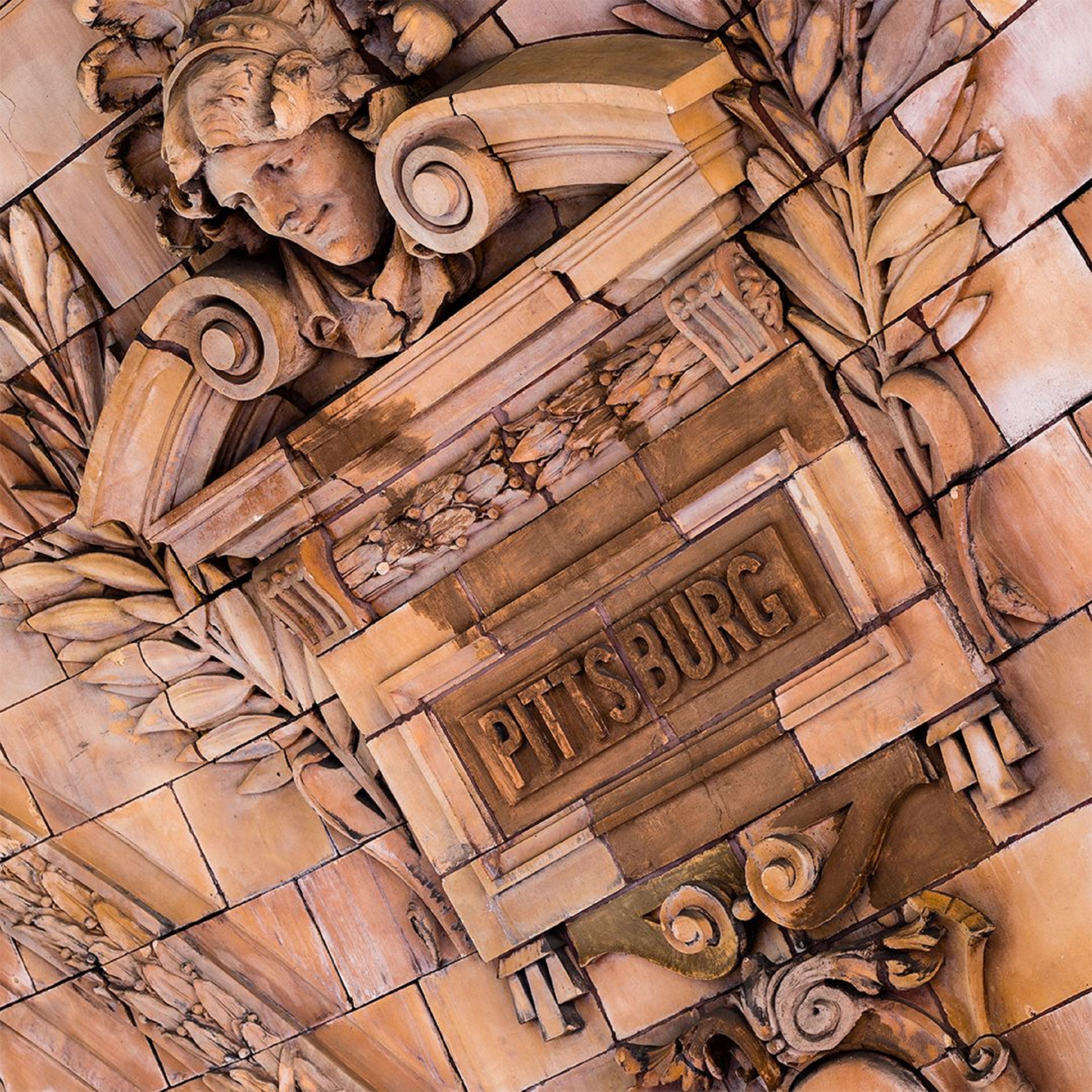 A detailed stone carving with the inscription "PITTSBURG" on a building facade.