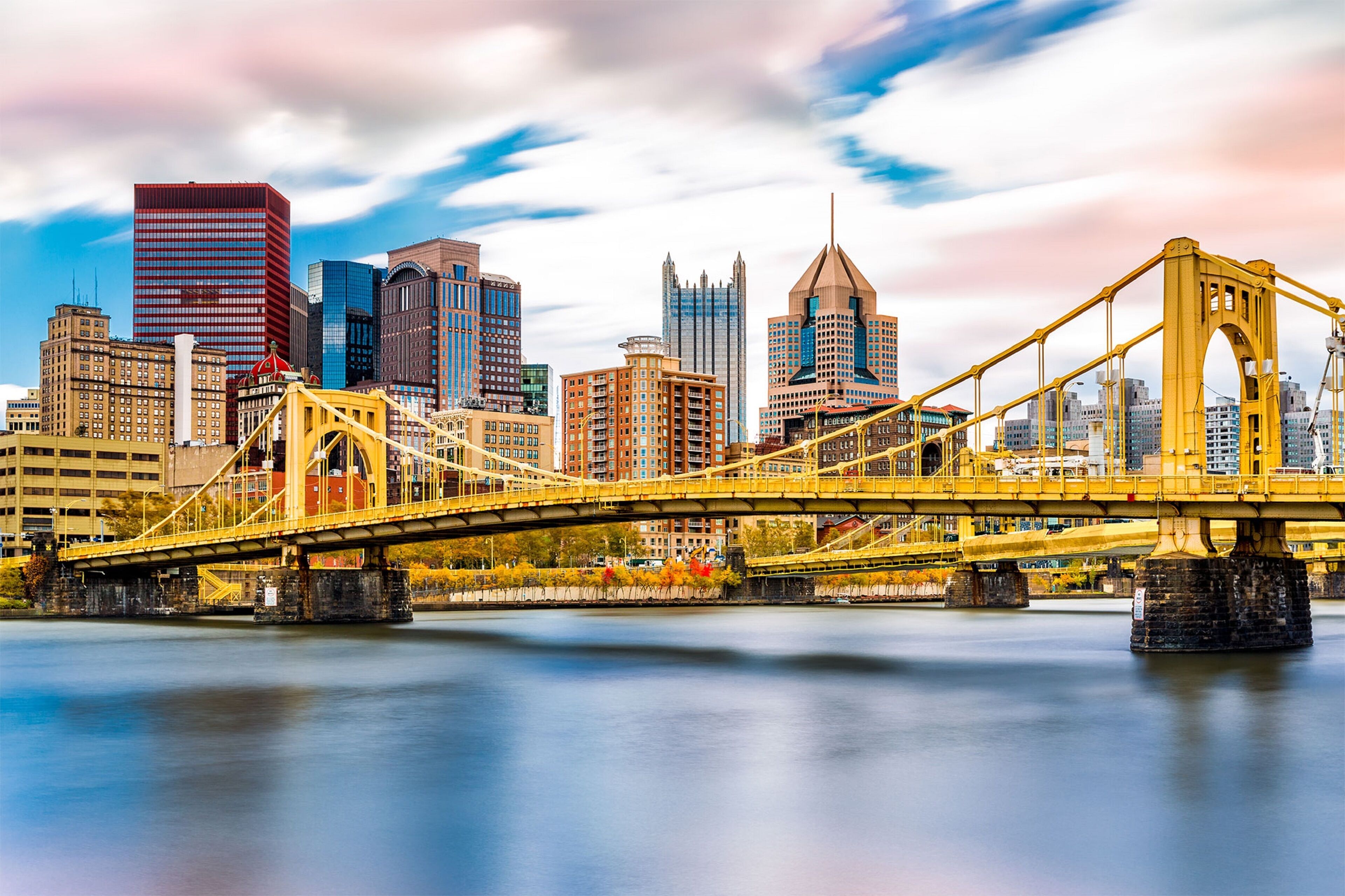 A yellow bridge spanning a river with a city skyline in the background.