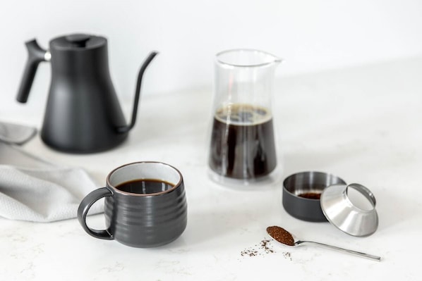 A coffee setup with a black coffee pot, a glass carafe, a mug, and a metal container with a lid.