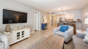 A living room with a TV, sofa, coffee table, and a kitchen area with a dining table and chairs. - Charming 2-bedroom Bayside T Model condo in Sarasota with courtyard views. (Sarasota)