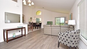 Un soggiorno moderno con un divano, una poltrona decorata, un'area da pranzo con sedie, un tavolo e un grande specchio.