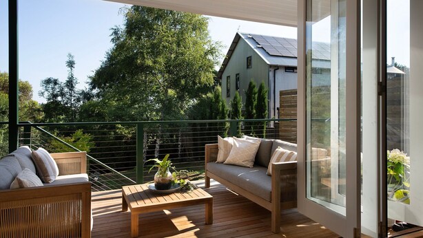 A wooden deck with a sofa and a table, a glass door, and a view of a house and trees. - Pembroke Cottage- modern comforts and scenic views (Daylesford)