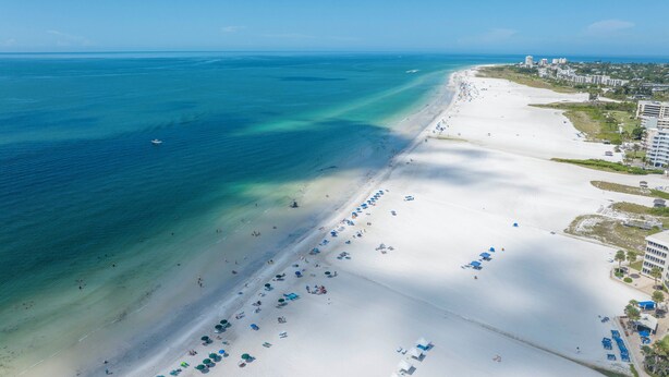 Oversigtsbillede af en strand med klart turkis vand, hvidt sand og en række strandparasoller.