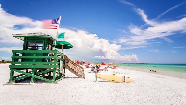 A lifeguard tower with a flag, a lifeguard chair, and a rescue board on a sandy beach with clear skies. - 2BD/2BTH apartment, fenced in yard.  10-minute drive to beautiful Siesta Beach.  (Sarasota)