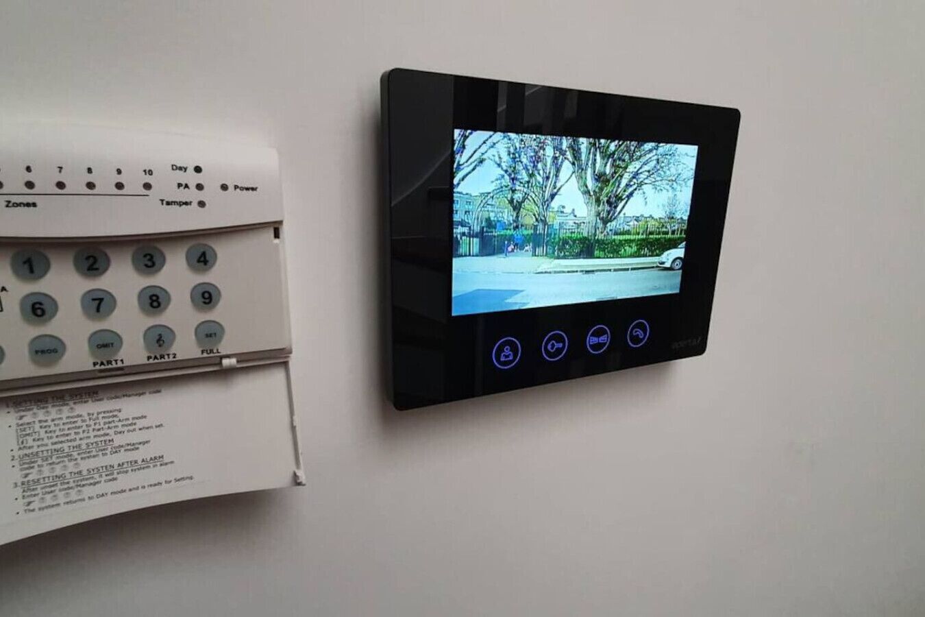A security system with a keypad and a screen displaying a view of a street.