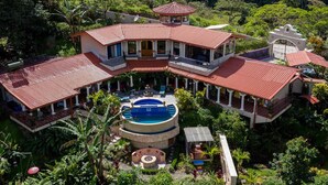 Una casa grande de varios niveles con una piscina central, rodeada de abundante vegetación.