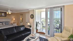 Una sala de estar con un sofá de cuero negro, una mesa de centro blanca, un sillón color beige y un balcón con vista a la ciudad.
