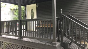 A wooden porch with a railing, a bench, and a door with a decorative glass window. - 1 bedroom/1 bath (Oneonta)