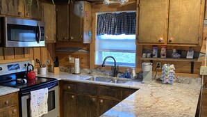Una cocina con armarios de madera, un microondas de acero inoxidable, una estufa y un lavamanos.