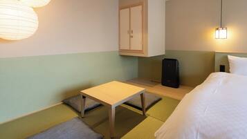 A hotel room with a bed, a small table, a cabinet, and a speaker.
