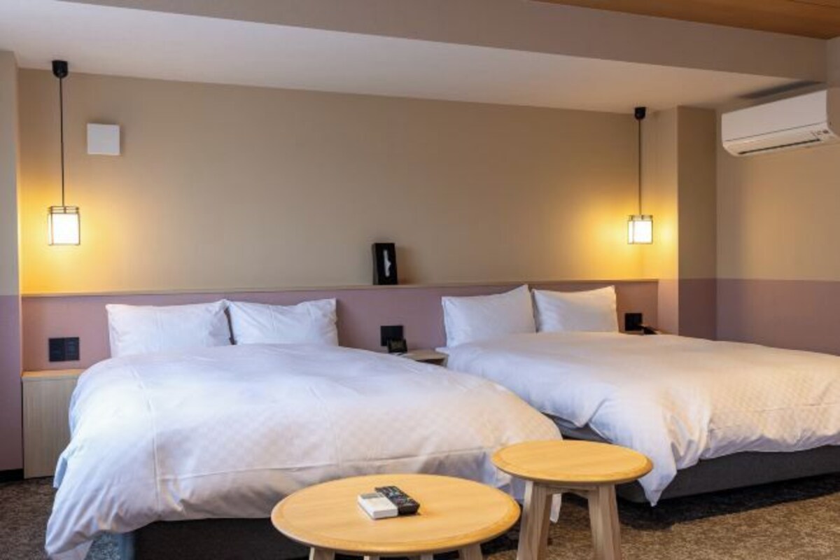 A hotel room with two beds, bedside tables, lamps, a clock, and an air conditioning unit.