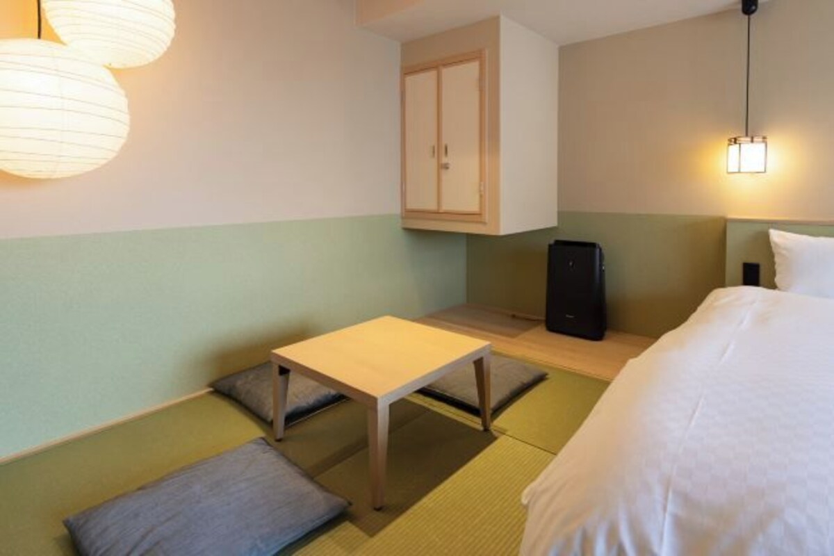 A hotel room with a bed, a small table, a cabinet, and a desk.